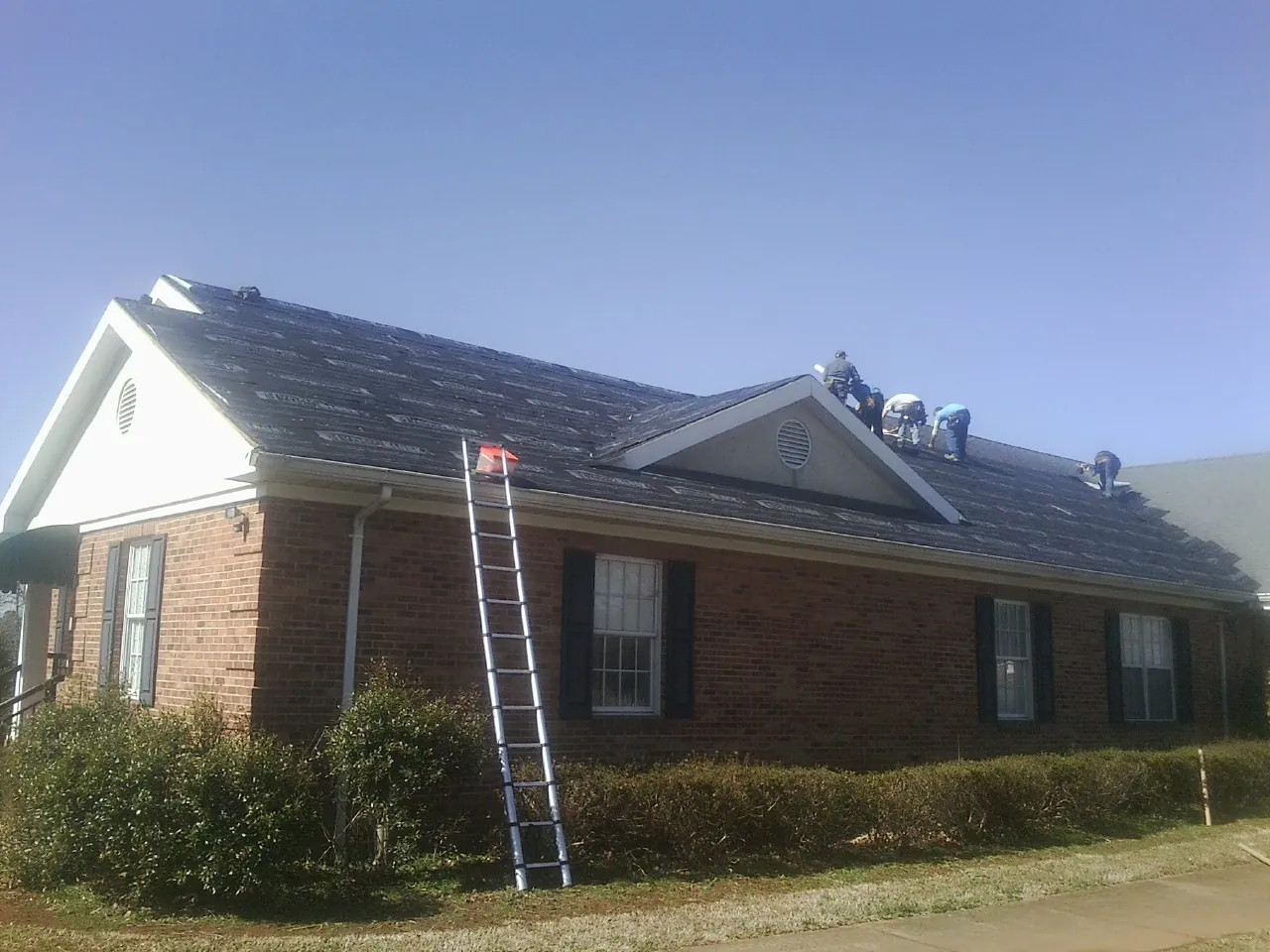 Crew tearing shingles off a brick ranch roof with a ladder set — Emergency Roof Repair work by our crew in Sauk Centre