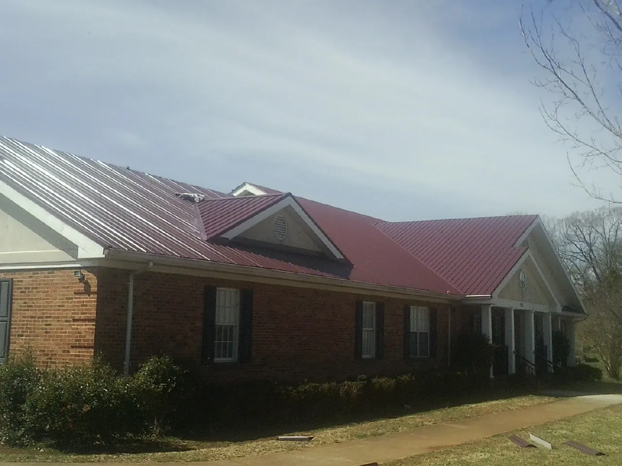 Red metal roof with gabled entries on a long brick building, from a Hail Damage Roof Repair job in Sauk Centre