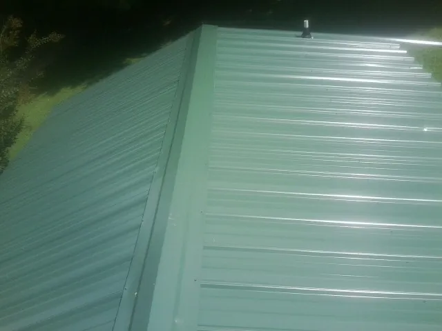 New green metal panels meeting at the ridge of a roof — Flat Roof Repair work by our crew in Sauk Centre