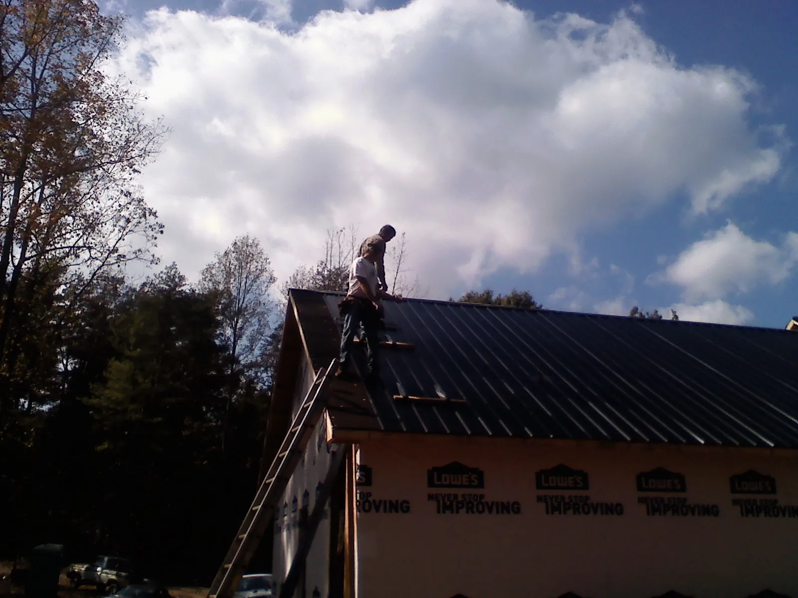 Roofer fastening dark metal panels high against a cloudy sky, from a Roof Inspection job in Sauk Centre