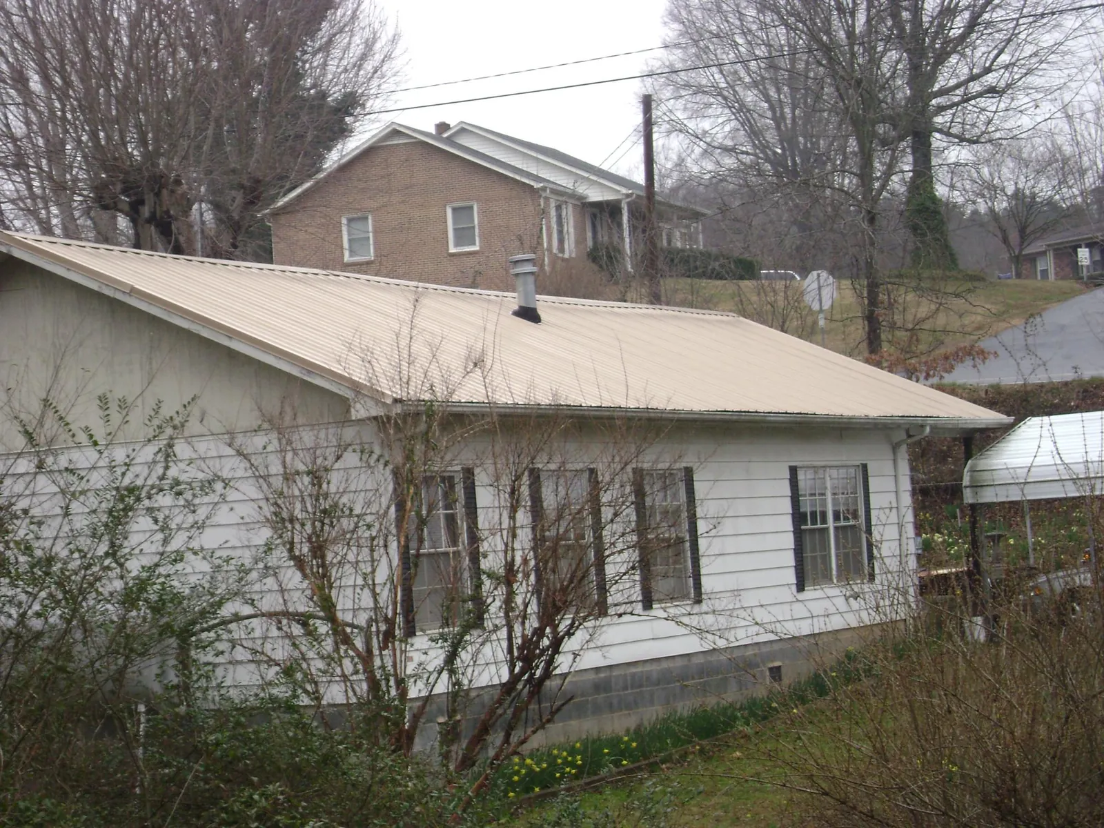 Tan metal roof on a white sided house set into a hillside — Commercial Roofing by Roofing Brothers in Sauk Centre