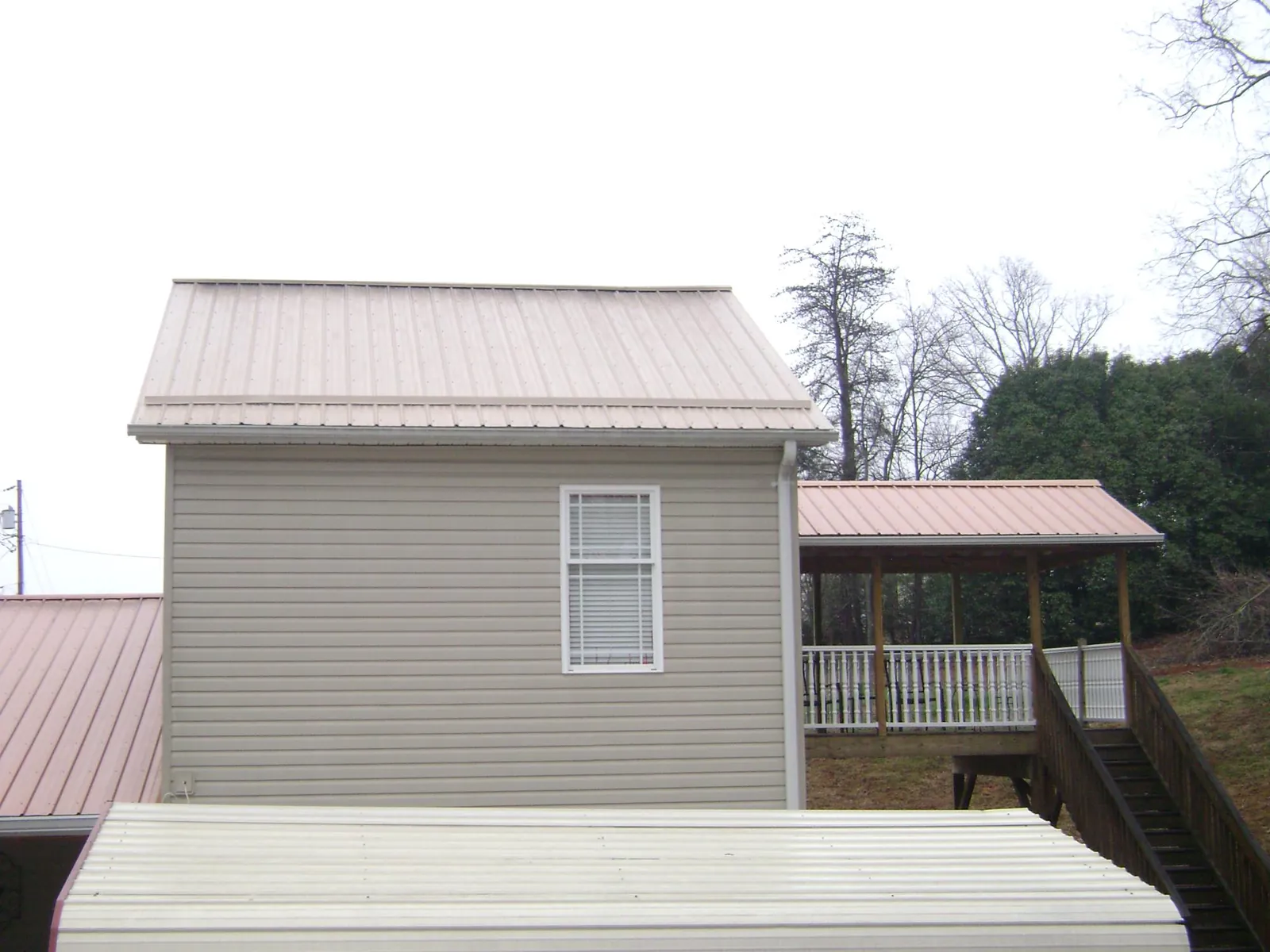 Tan metal roofs on a two story addition and attached porch, from a Roof Replacement job in Sauk Centre