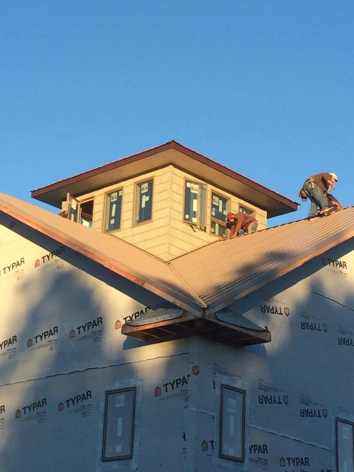 Roofers working around a rooftop cupola on a new metal roof at sunset — Roof Waterproofing in Sauk Centre by Roofing Brothers
